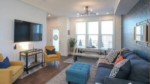 A modern living room with a sofa, armchairs, a coffee table, and a TV mounted on the wall.