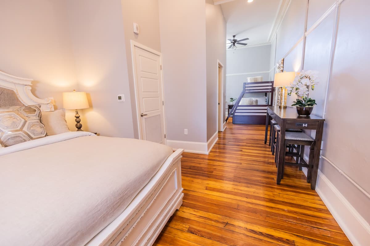 Quarto de hotel com uma cama grande, piso de madeira, uma mesa com luminária e escada que leva a outro cômodo.