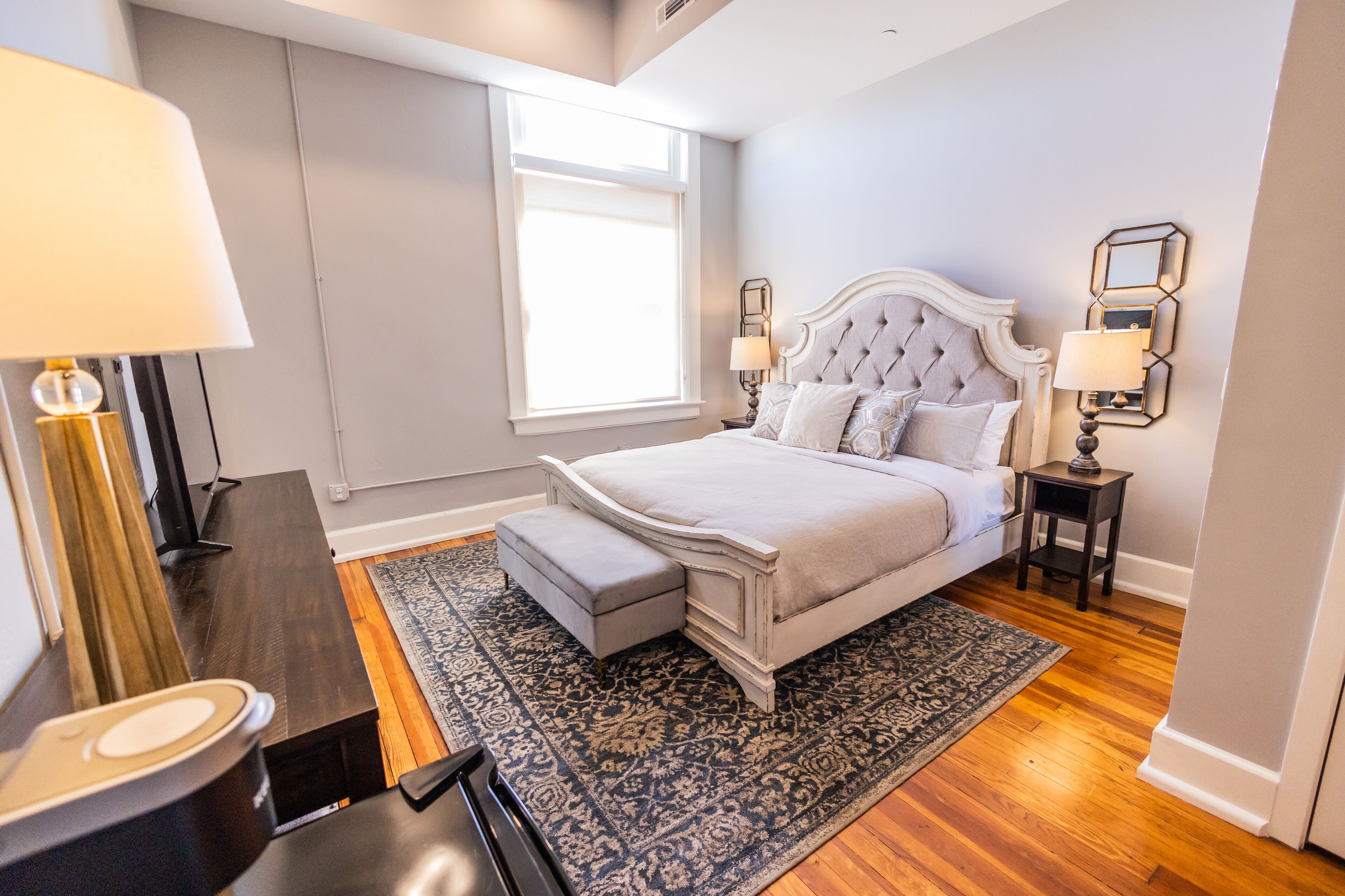 A bedroom with a large bed, a nightstand, a lamp, and a window.