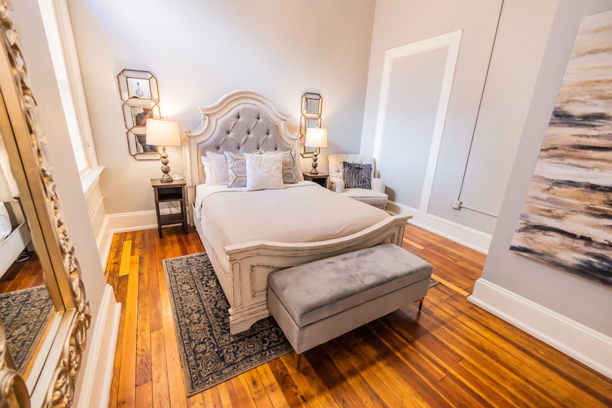 Quarto com uma cama grande, duas mesas de cabeceira, um banco, um tapete e um quadro na parede.