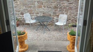 A patio with two white chairs and a round table, set against a stone wall. - Ground Floor Cornish Retreat and Courtyard Garden (Bodmin)