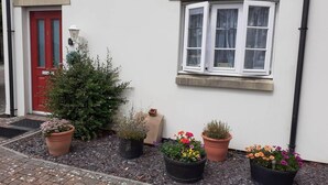 A white building with a red door, a small Christmas tree, and four flower pots with various plants. - Ground Floor Cornish Retreat and Courtyard Garden (Bodmin)