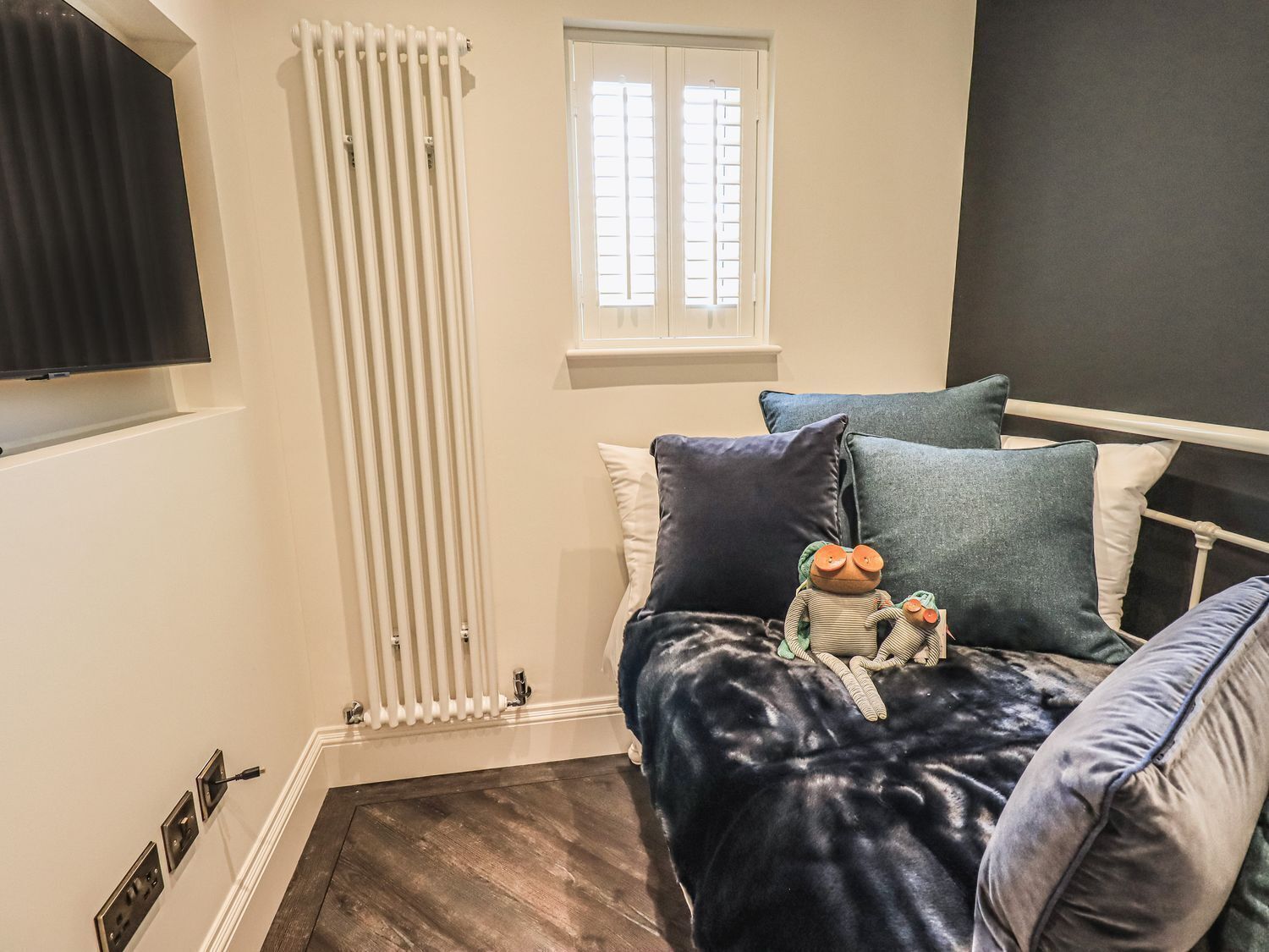 Un dormitorio con cama, un radiador, una ventana y un televisor montado en la pared.