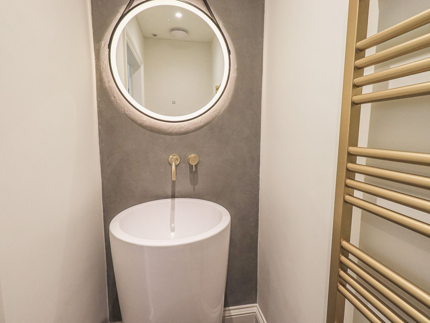 Une salle de bain avec un lavabo sur colonne, un miroir rond et un porte-serviettes.