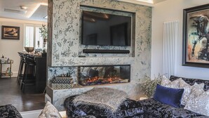Un salon doté d’une cheminée, d’un grand téléviseur fixé à un mur à texture et d’un ensemble de meubles de salon modernes.