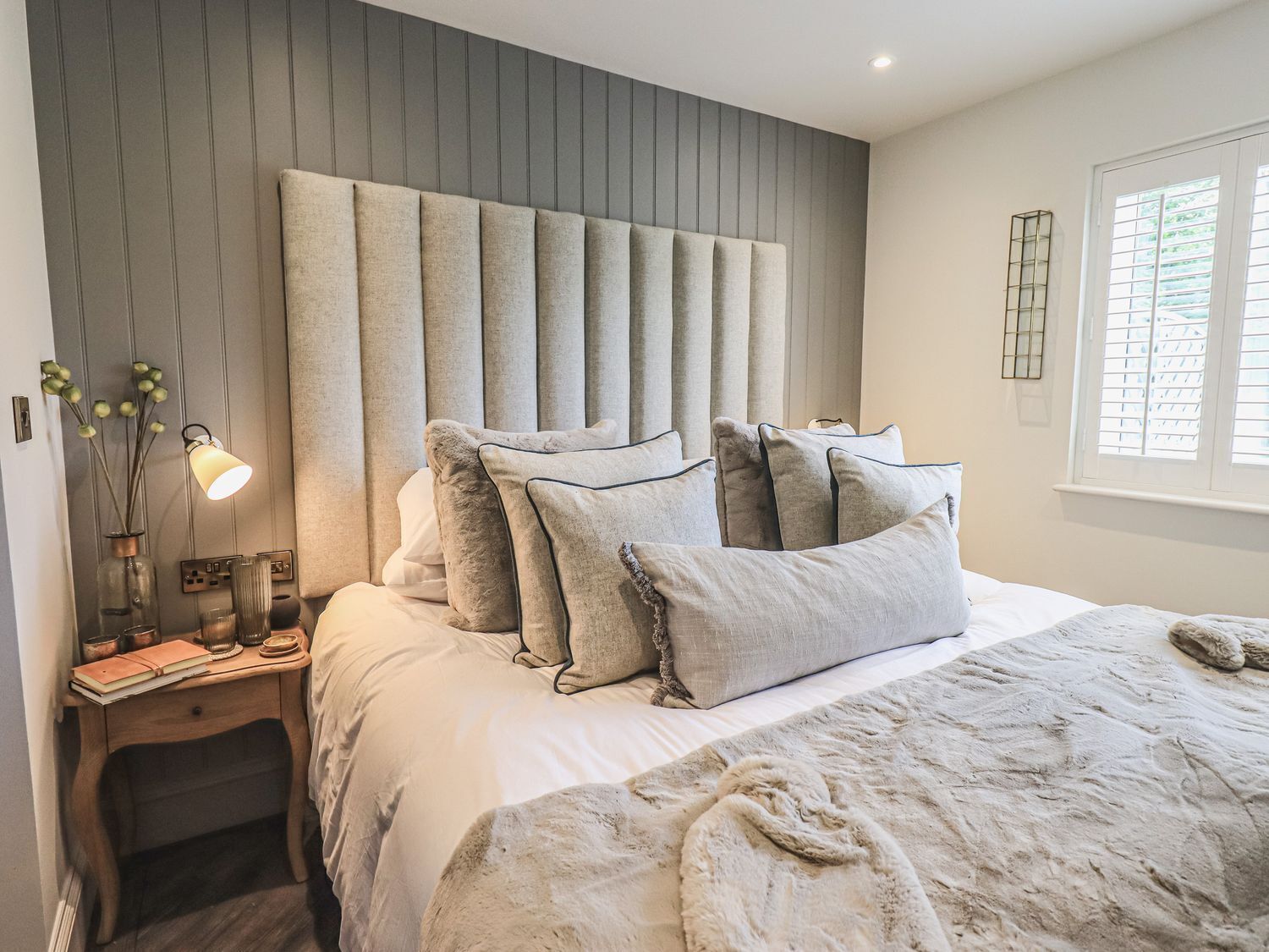 A bedroom with a large bed, a bedside table with a lamp, and a window with blinds.