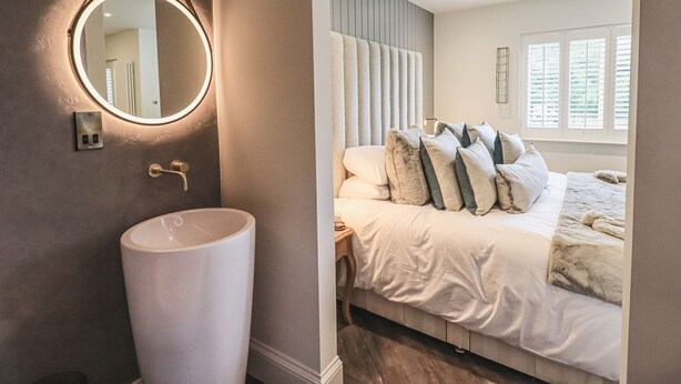 Une chambre moderne avec un grand lit, un miroir rond et un lavabo blanc.