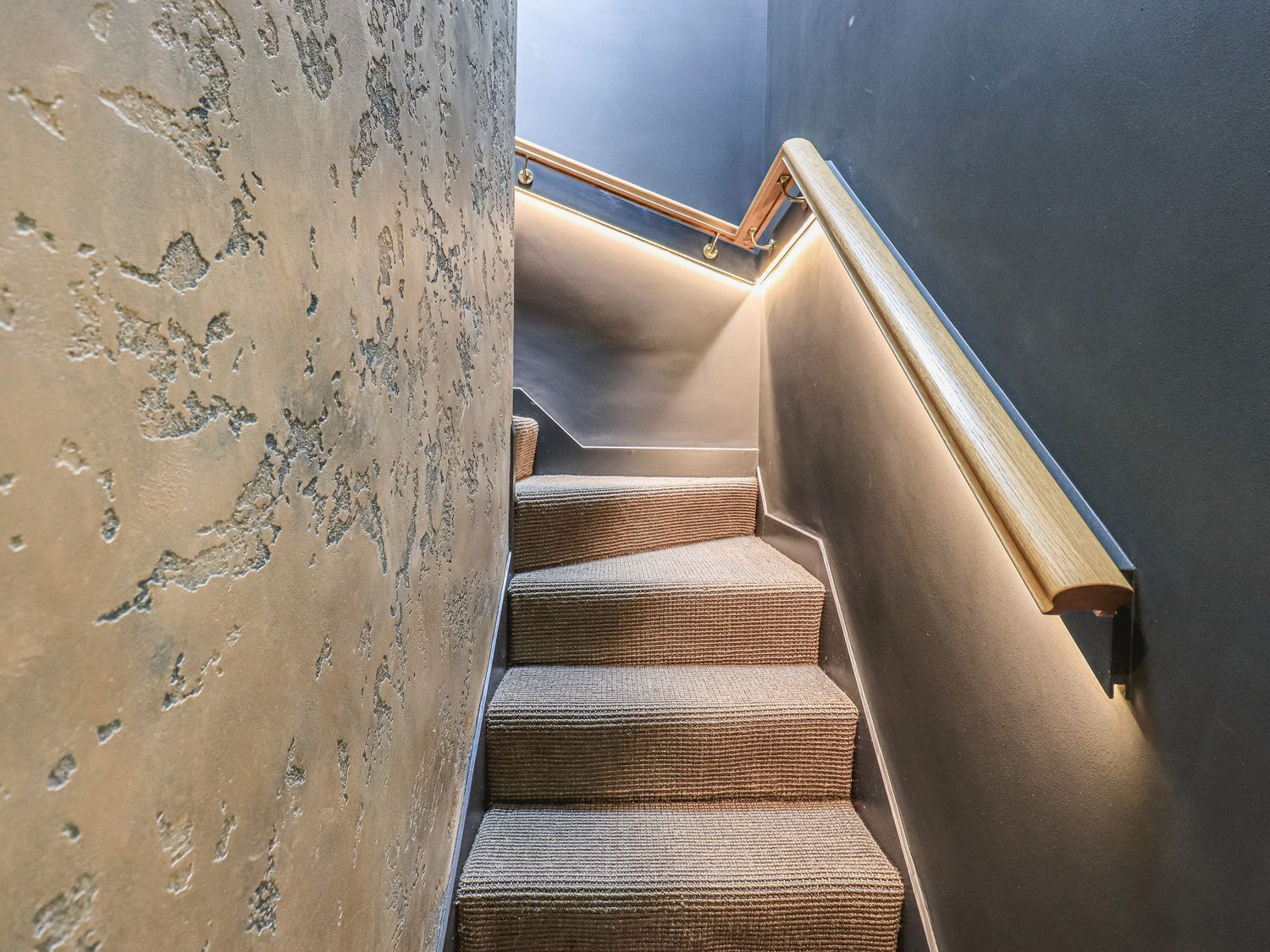 Un escalier avec un mur à texture et une main courante en bois.
