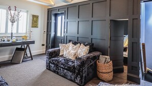 Un salon moderne avec un canapé aux couleurs sombres, un bureau agrémenté d’un vase de fleurs et une grande fenêtre.