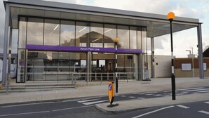 Ein modernes Gebäude mit Glasfassade und einem violetten Vordach, auf dem "Acton Main Line" steht.