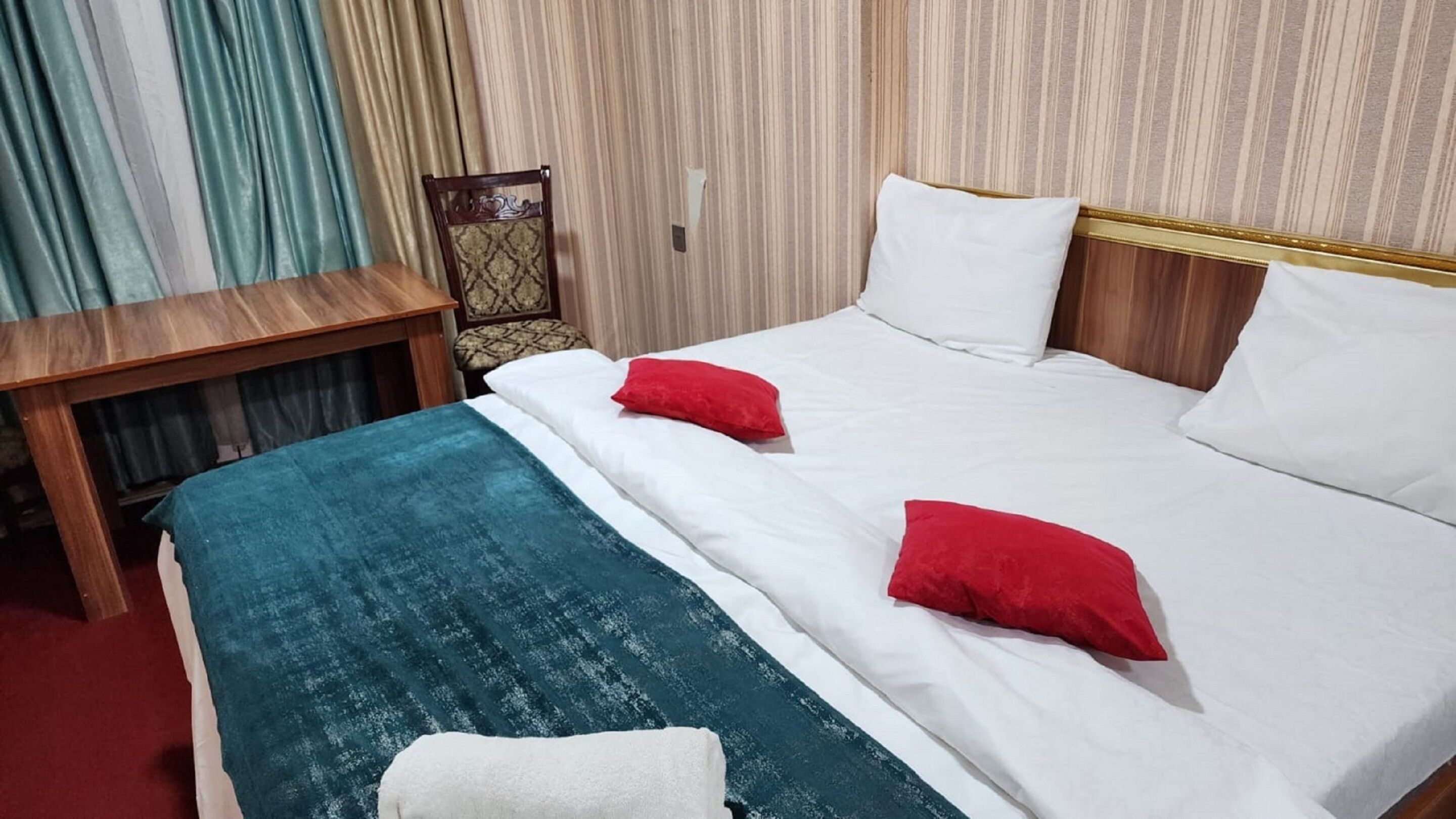 A hotel room with a bed, two pillows, a bedside table, and a chair.