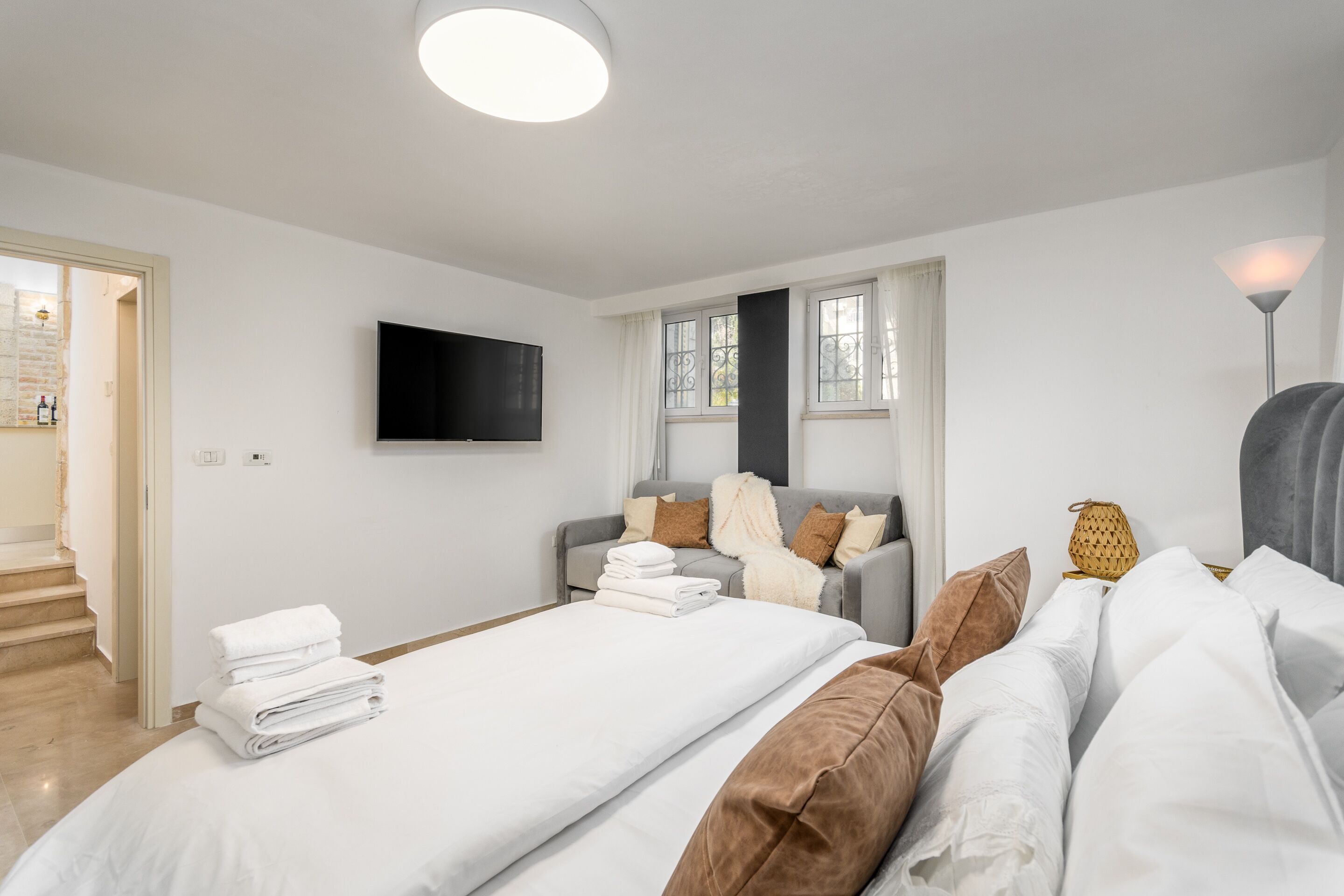 A modern hotel room with a large bed, a sofa, and a TV mounted on the wall.