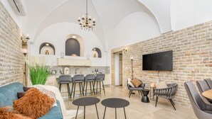 A spacious living area with a blue sofa, two round tables, and a kitchen in the background. - Nina Luxury Apartment (Jerusalem)