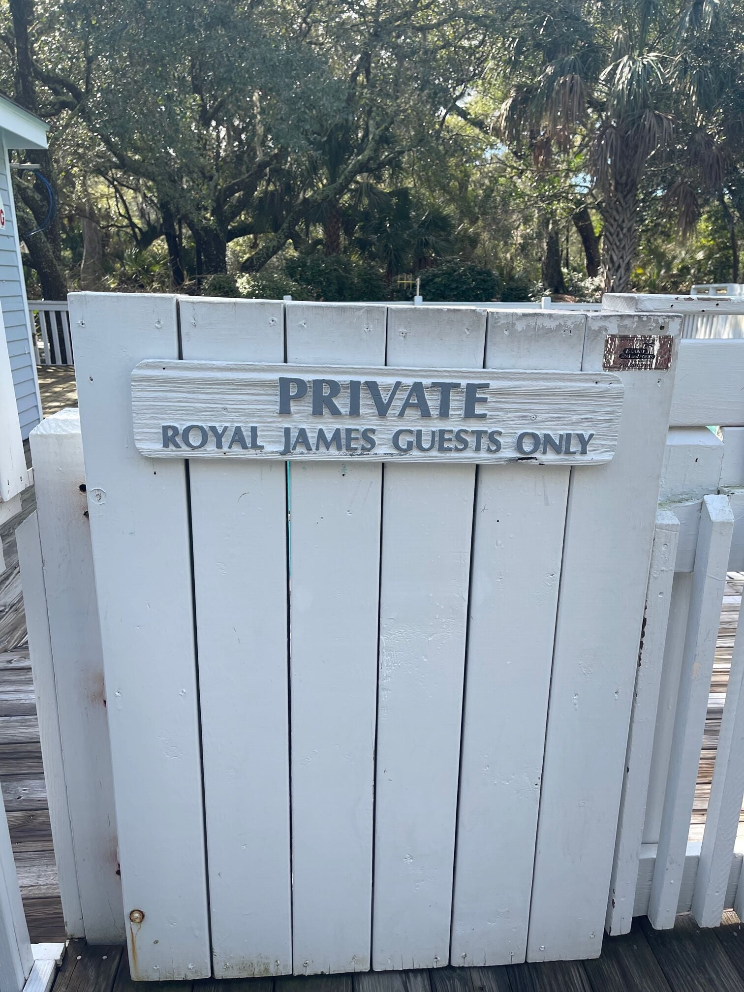 Ein weißes Holztor mit einem Schild, auf dem steht: 'PRIVATE ROYAL JAMES GUESTS ONLY'.