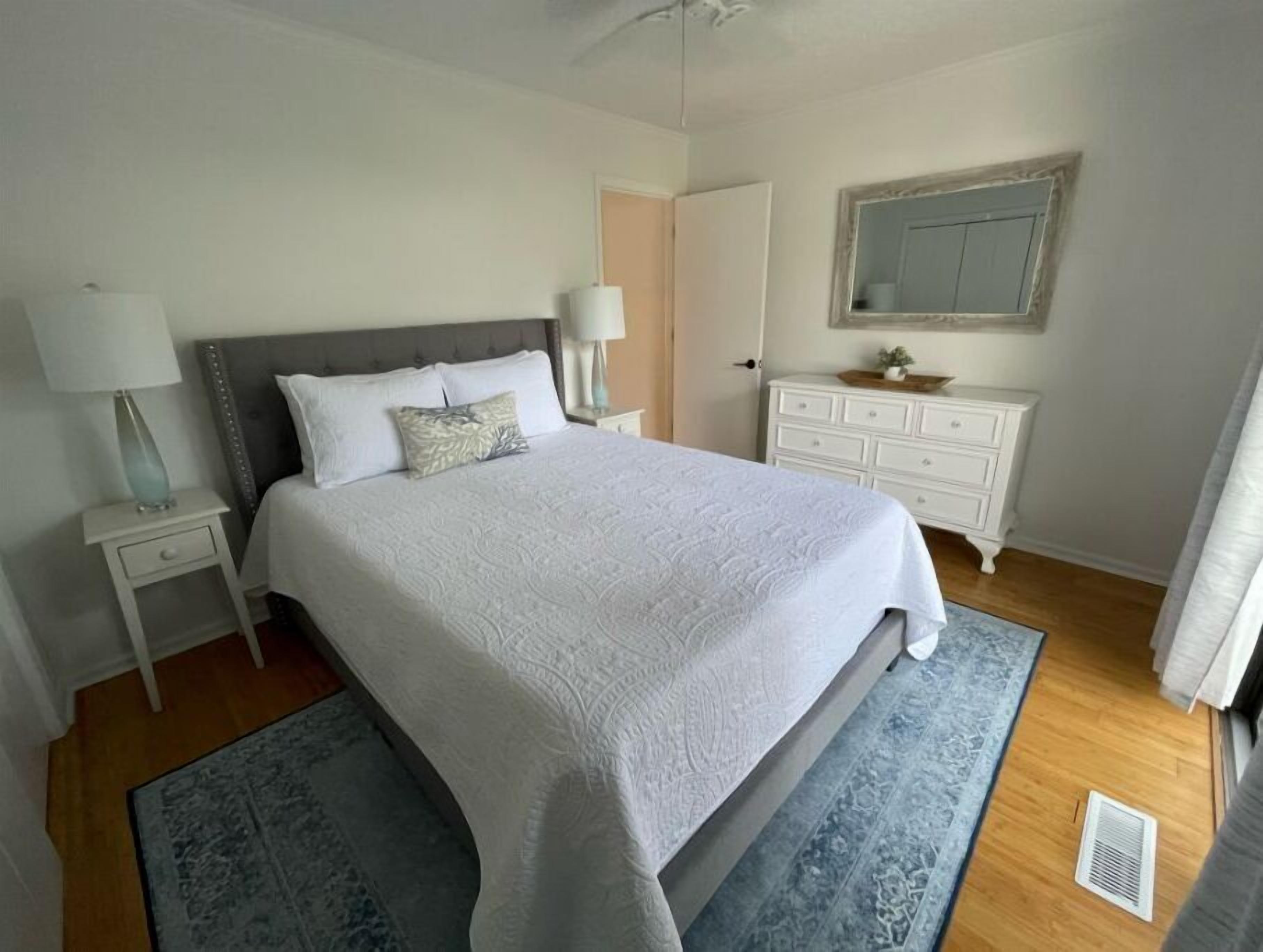A neatly arranged bedroom with a large bed, two bedside tables with lamps, a dresser, and a mirror on the wall.