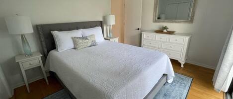 A neatly arranged bedroom with a large bed, two bedside tables with lamps, a dresser, and a mirror on the wall.