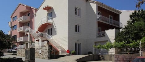 A multi-story residential building with balconies, a central staircase, and a red car parked in front.