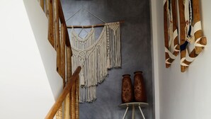 A staircase with a wooden handrail, a macrame wall hanging, and two vases on a small table. - POUSADA SOLE - D3 EXPERIENCE (Cruz)