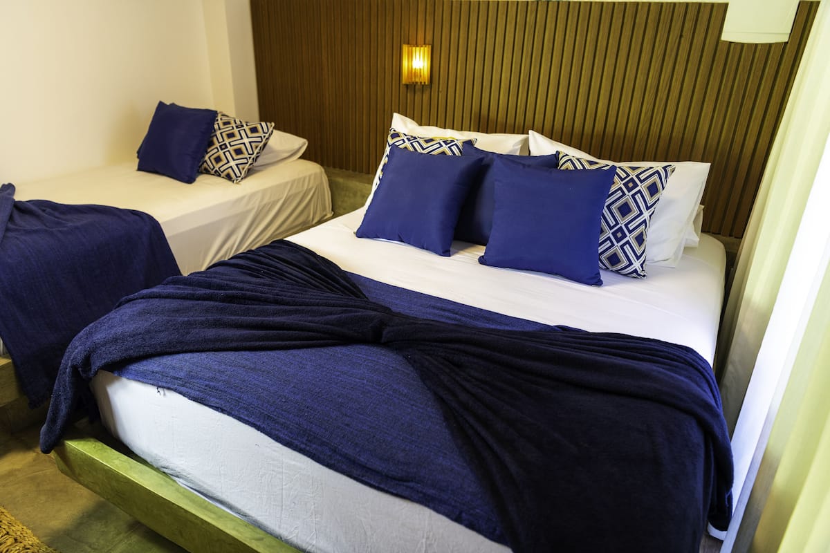 Une chambre d’hôtel avec deux lits simples, chacun agrémenté d’un coussin à motifs et d’une couverture bleue.
