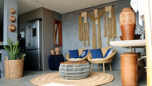 A modern living room with a sofa, a round woven coffee table, a refrigerator, and decorative wall hangings. - POUSADA SOLE - D3 EXPERIENCE (Cruz)
