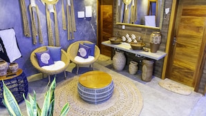 A room with a blue and gold color scheme, featuring wicker furniture, a round wooden table, and decorative items on shelves. - POUSADA SOLE - D3 EXPERIENCE (Cruz)