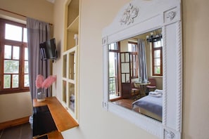 Une chambre avec un grand miroir, une télévision, un bureau en bois et une fenêtre avec des rideaux.