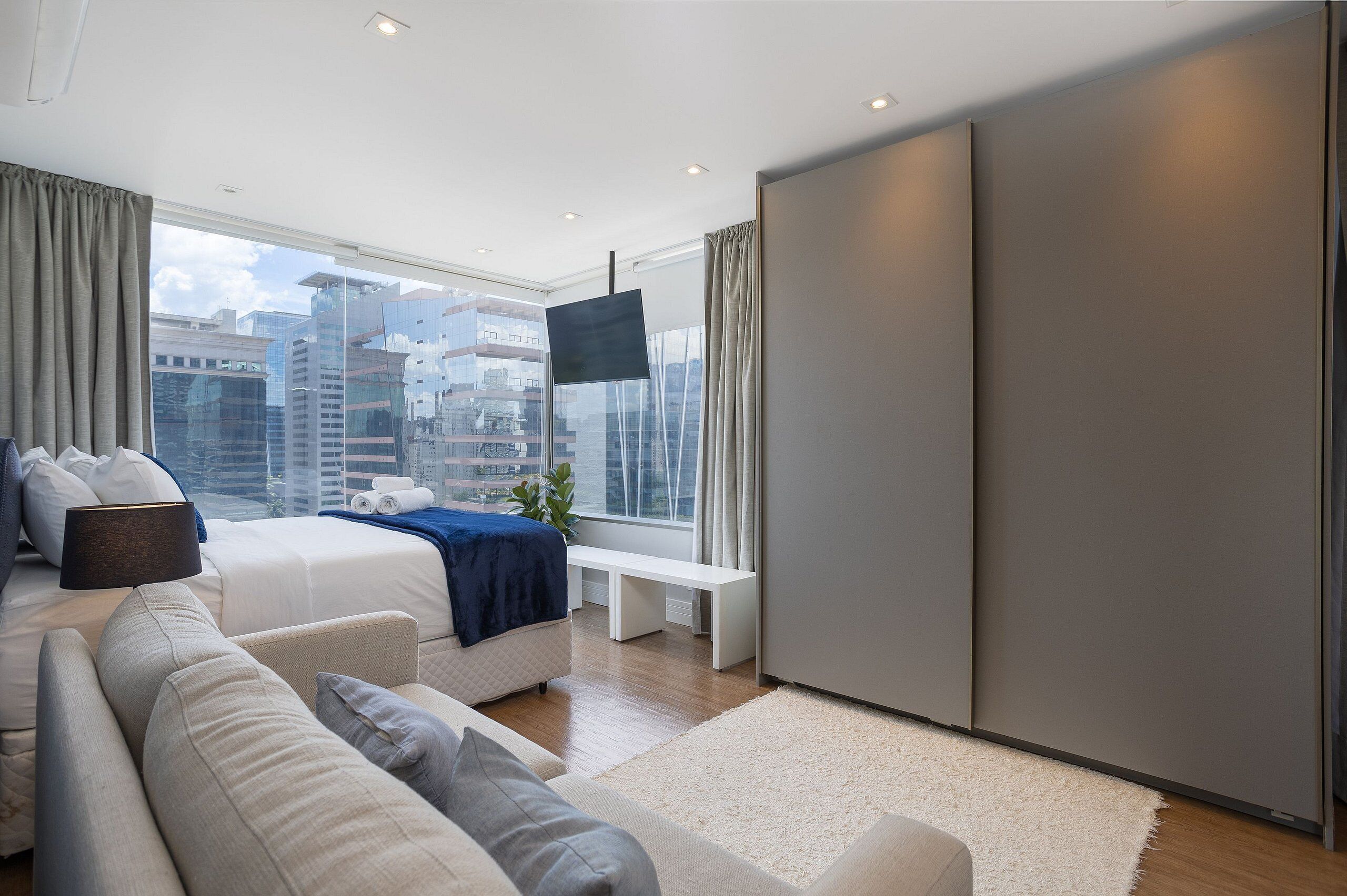 A modern bedroom with a bed, sofa, and a large window with a city view.