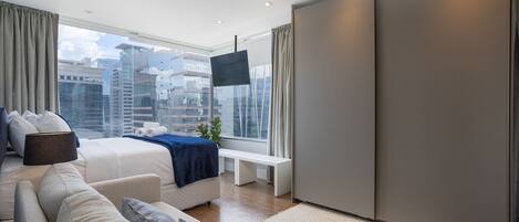 A modern bedroom with a bed, sofa, and a large window with a city view.