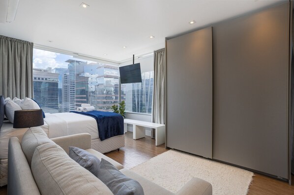 Une chambre moderne avec un lit, un canapé et une grande fenêtre donnant sur la ville.