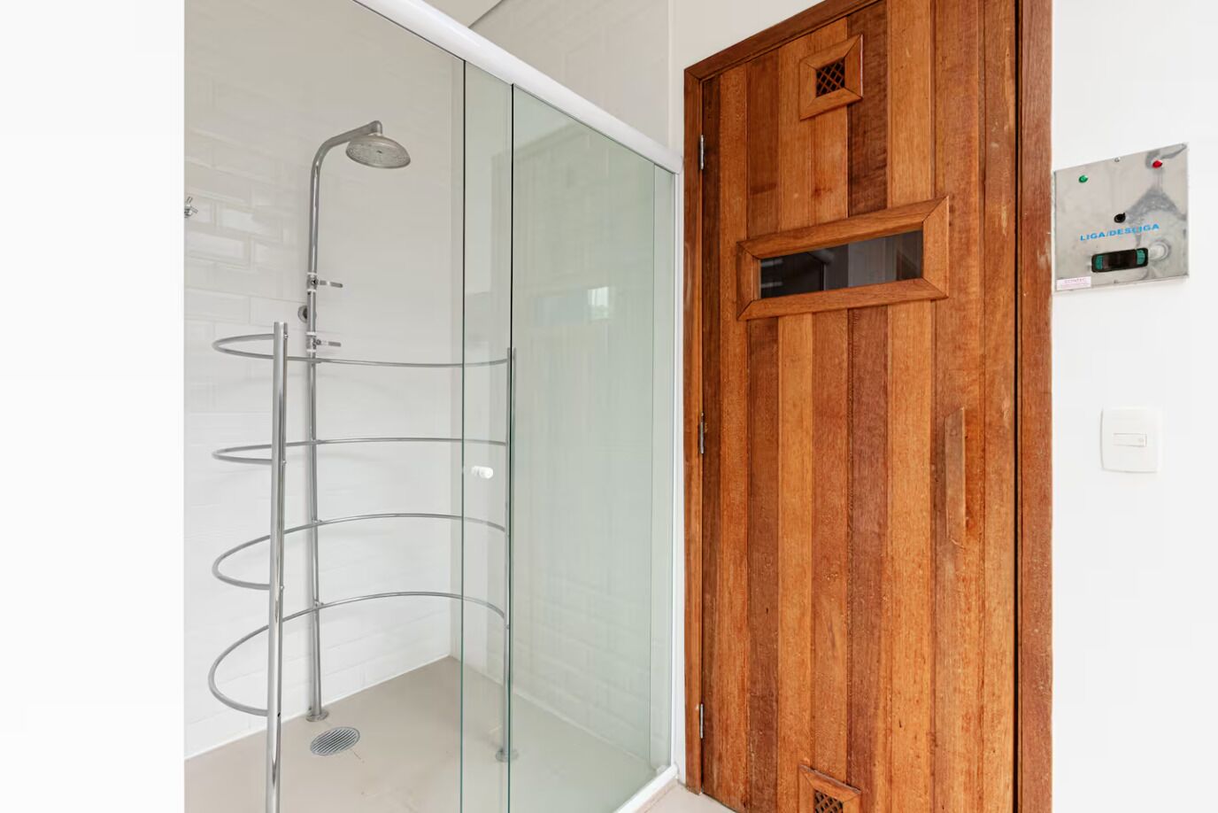 A bathroom with a glass shower enclosure, a wooden door, and a wall-mounted control panel.