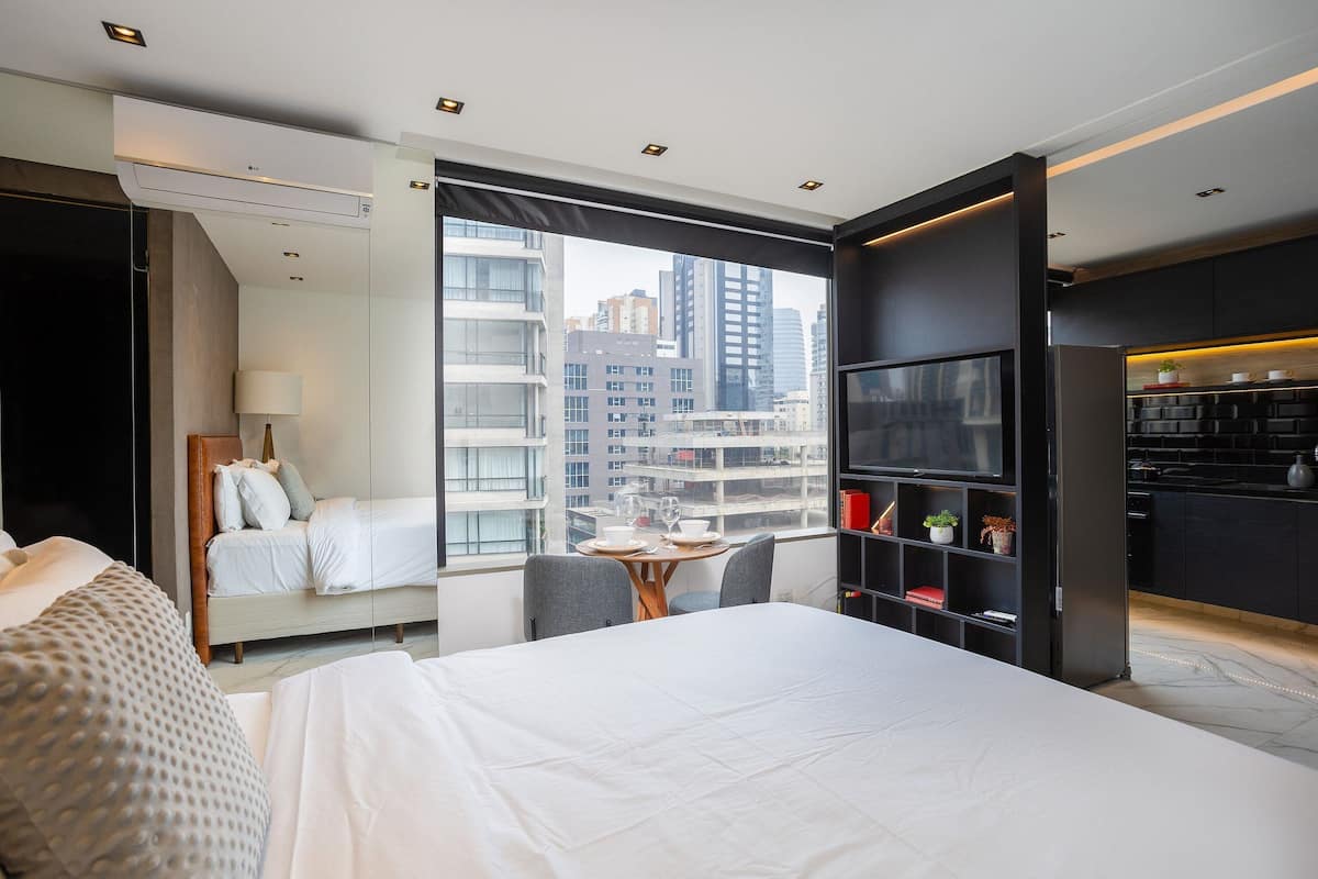 Een moderne hotelkamer met een bed, een eettafel, een televisie en uitzicht op de skyline.