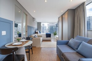 A modern hotel room with a dining area, a sofa, a bed, and a view of the city.