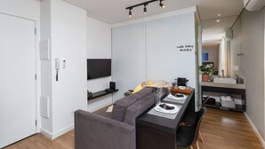 En moderne stue med sofa, spisebord, fjernsyn og et køkkenområde med vask og bordplade.