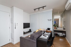 A modern living room with a sofa, a dining table, a TV, and a kitchen area with a sink and countertop. - VN Ferreira Lobo (São Paulo)