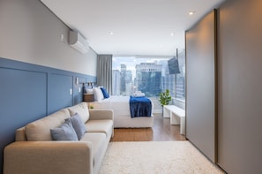 Een moderne hotelkamer met een bed, een bank, een televisie en uitzicht op de stad.