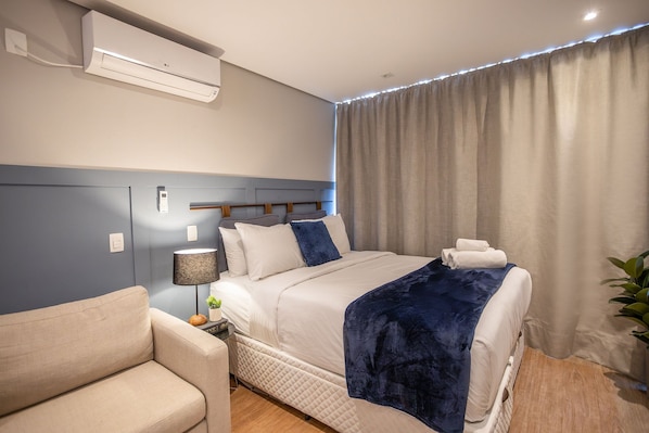 A modern hotel room with a bed, a bedside table, a lamp, and a wall-mounted air conditioner.