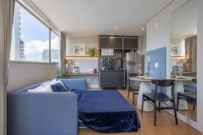 Een compacte hotelkamer met een bed, een klein kitchenette, een eethoek en een groot raam.