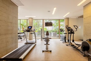 A gym with treadmills, elliptical machines, and a stationary bike, with large windows and a flat ceiling.