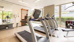 Et fitnessrum med løbebånd, vægtbænk og vægmonteret træningsmaskine.