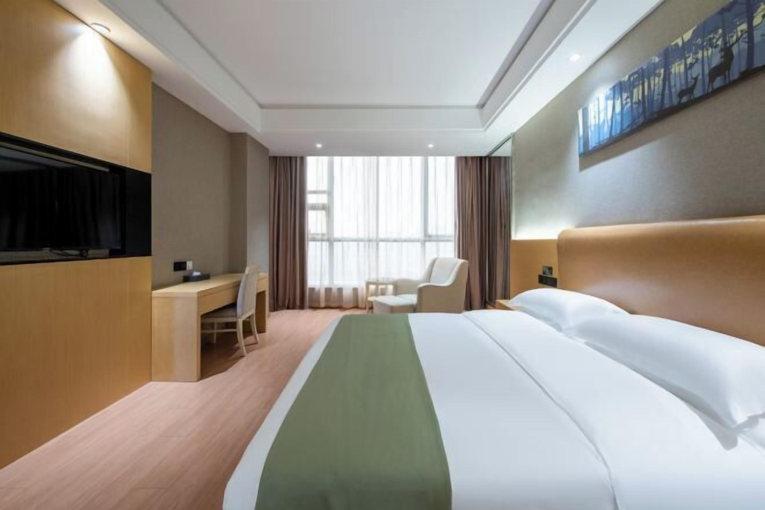 Une chambre d’hôtel avec un lit, un bureau, une chaise, une télévision et une fenêtre avec des rideaux.