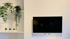Een moderne woonkamer met een wandgemonteerde flatscreen televisie, een kleine tafel met een lamp en een decoratieve vloerlamp.