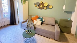Een woonkamer met een bank, een ronde salontafel met planten, een wand met decoratieve borden en een radiator.