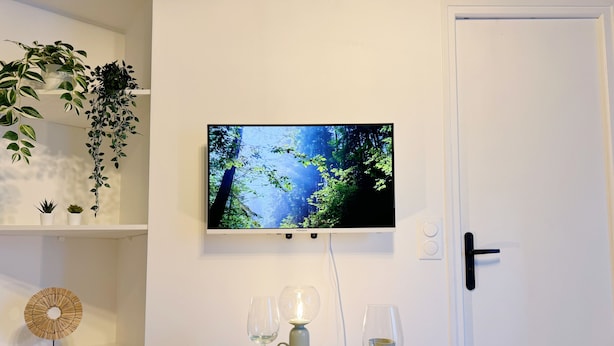 Een eetgedeelte met een tafel gedekt voor twee personen, een aan de muur bevestigde televisie, en een deur met een modern handvat.