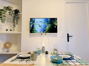 Ein Essbereich mit einem für zwei Personen gedecktem Tisch, einem an der Wand befestigten Fernseher und einer Tür mit einem modernen Griff.
