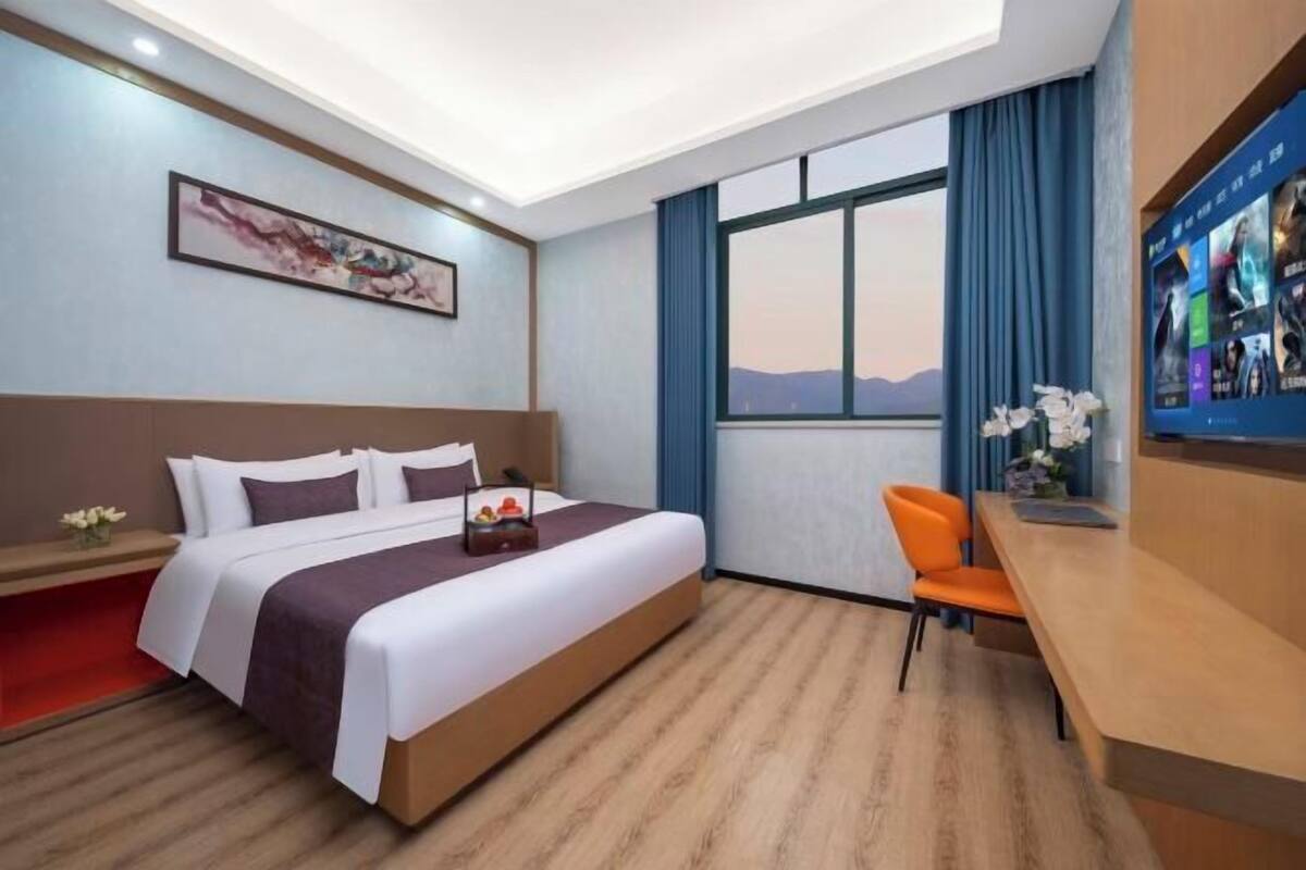 A hotel room with a bed, a desk, a TV, a window with a view, and a painting on the wall.