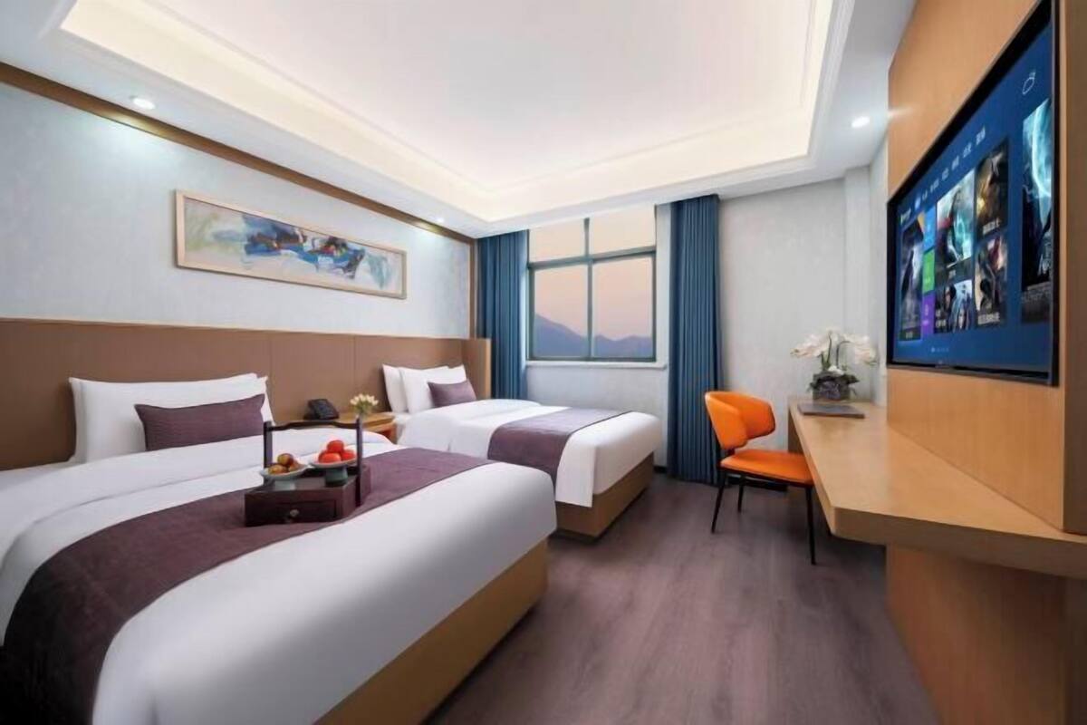 A hotel room with two beds, a desk, a chair, a TV, and a window with a view.