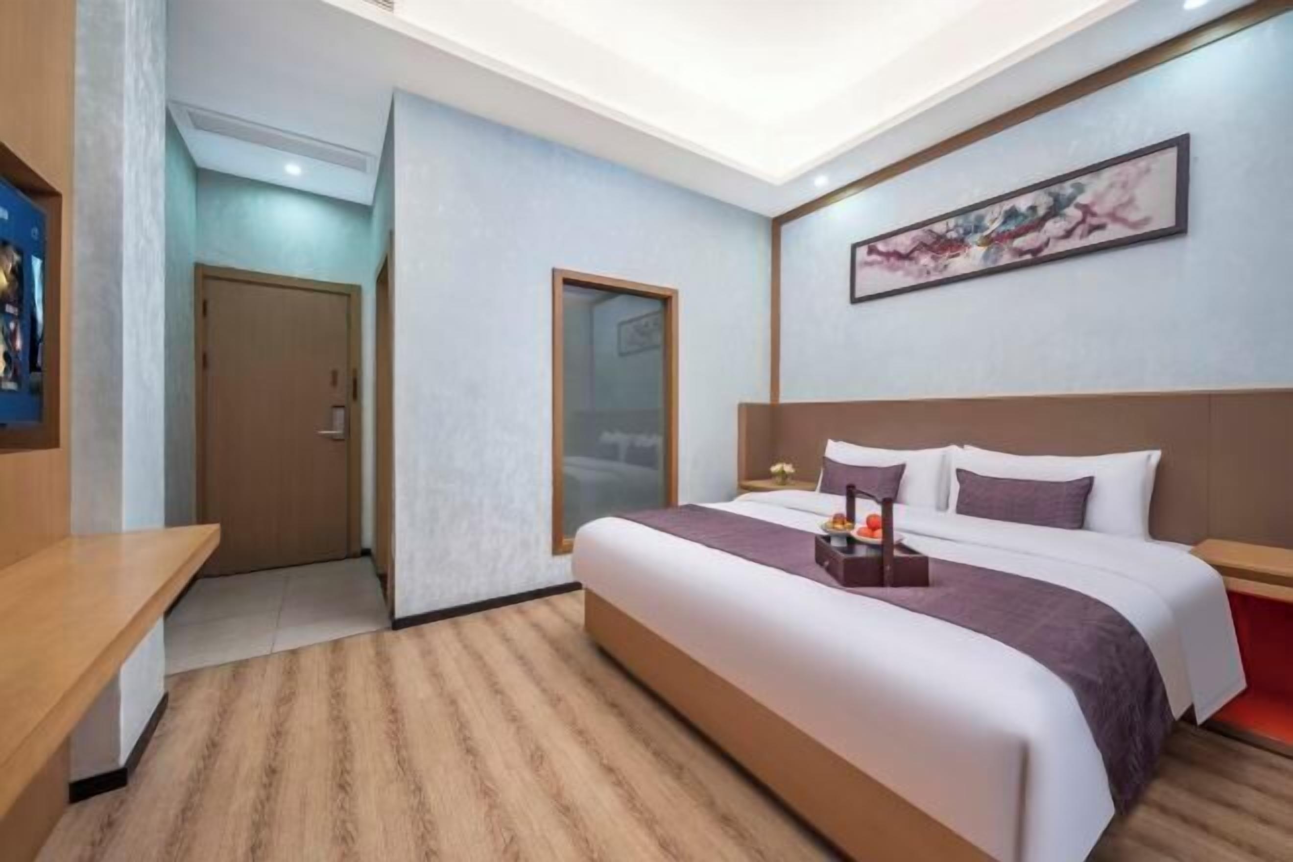 A hotel room with a large bed, a desk, and a painting on the wall.