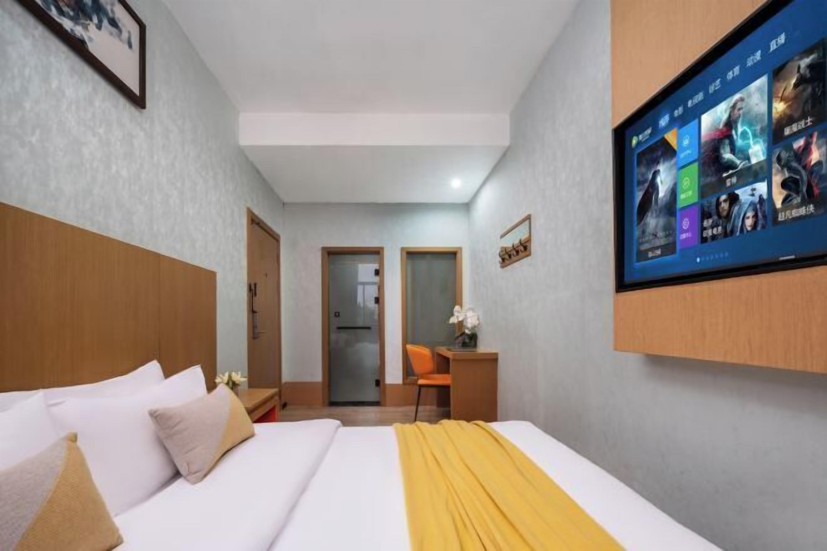 Habitación de hotel con cama, escritorio, silla y televisor en la pared mostrando carteles de películas.