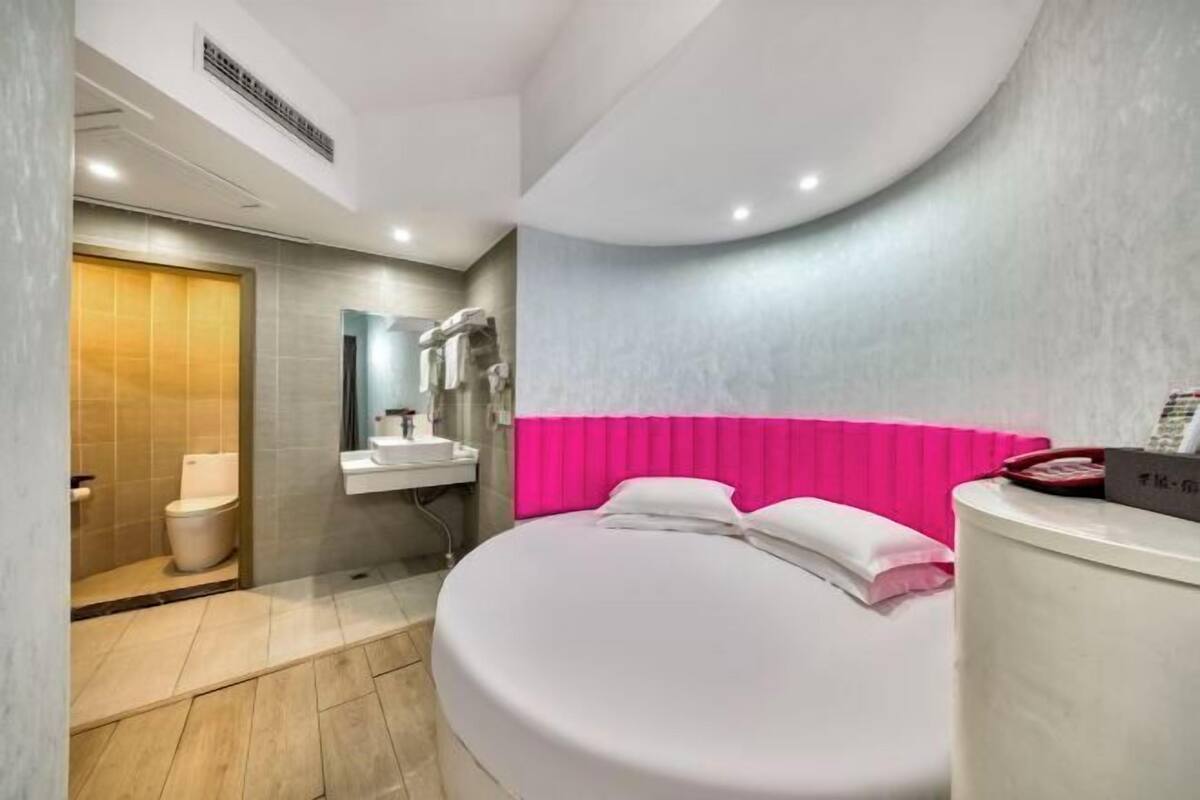 A modern hotel room with a large bed, a bathroom with a toilet and sink, and a shower area.