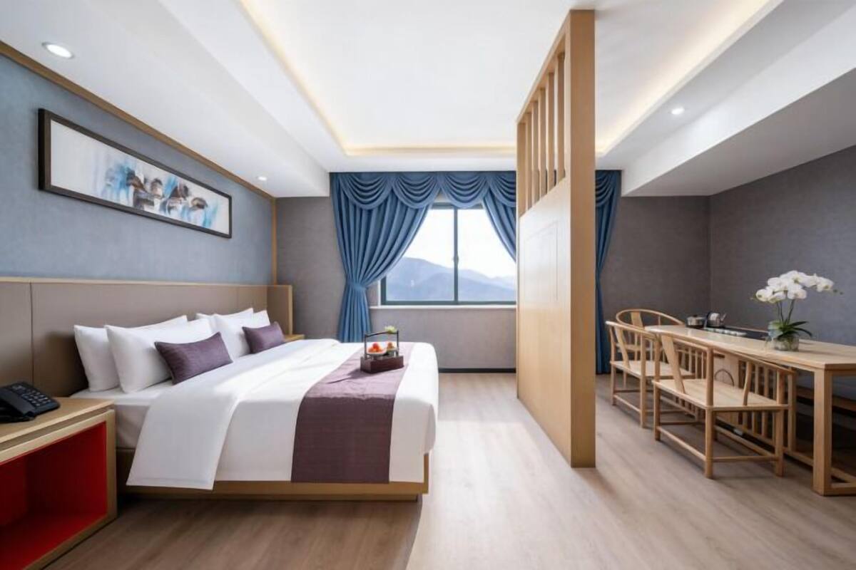 A hotel room with a bed, bedside table, desk, chairs, and a window with curtains.